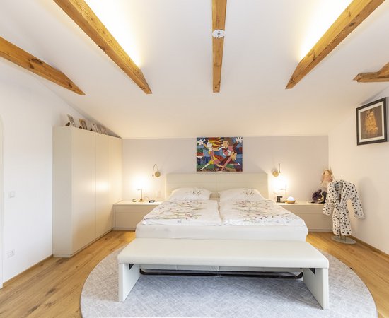 Schlafzimmer mit beleuchteten Deckenbalken aus Holz.
